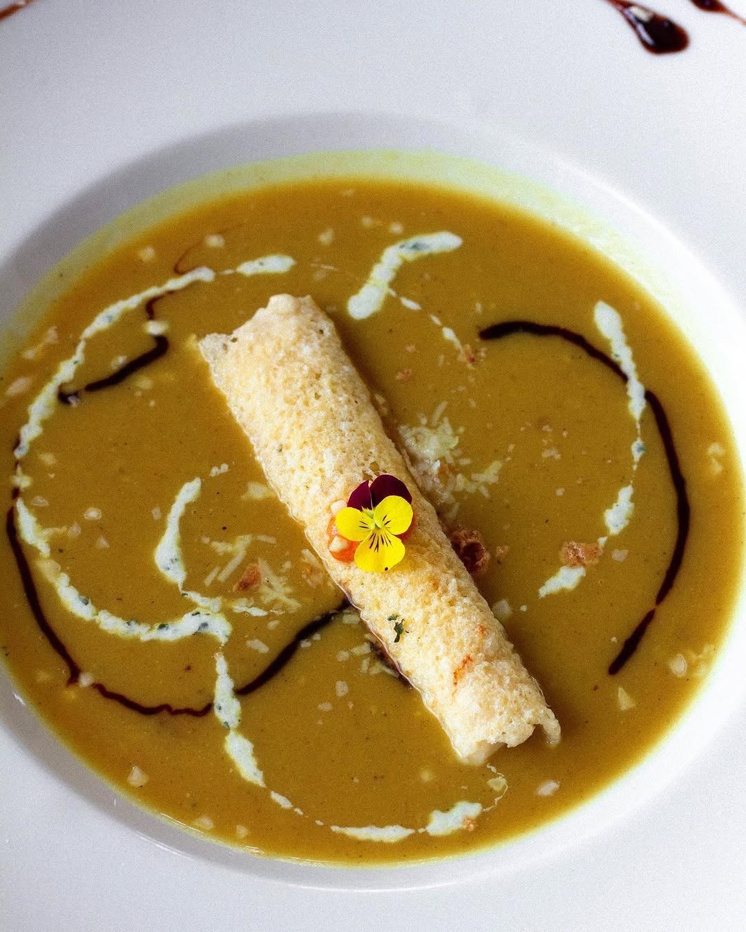 Creme amarelo num prato fundo branco, com um enrolado estaladiço e uma flor comestível